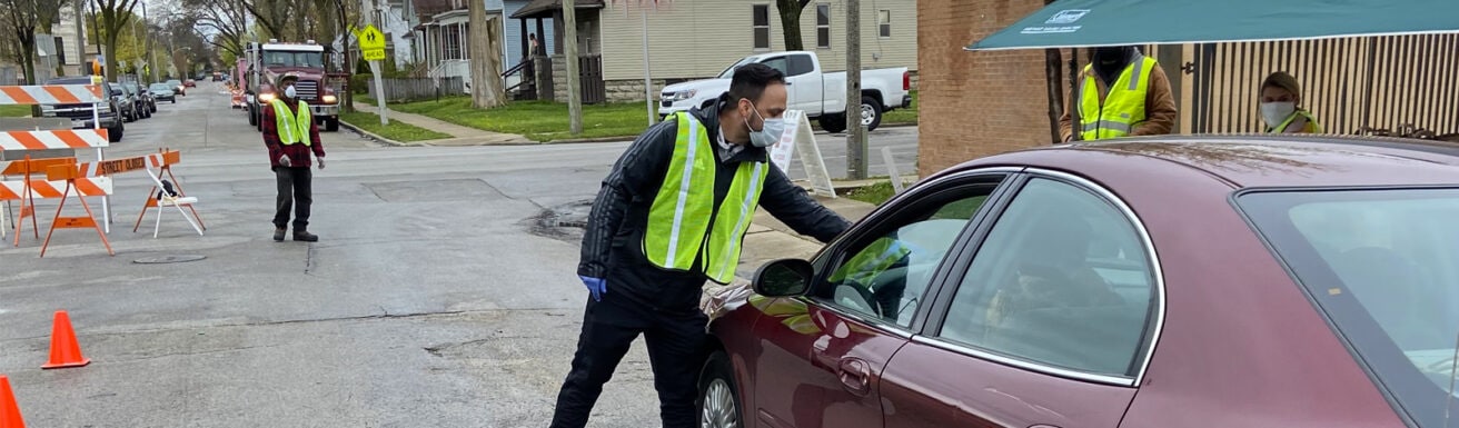 person in mask taking card off of a car windshield