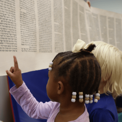 A group of children looking at a large scroll.