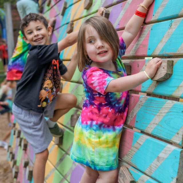 Two children climbing on a colorful wall.