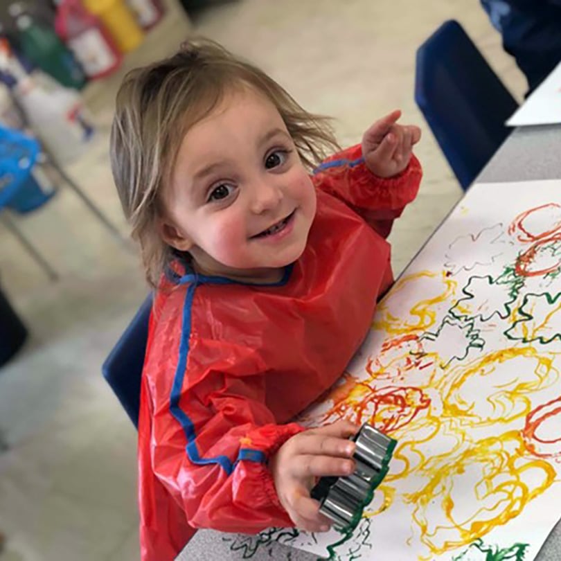 A little girl in a red coat is painting a piece of paper.