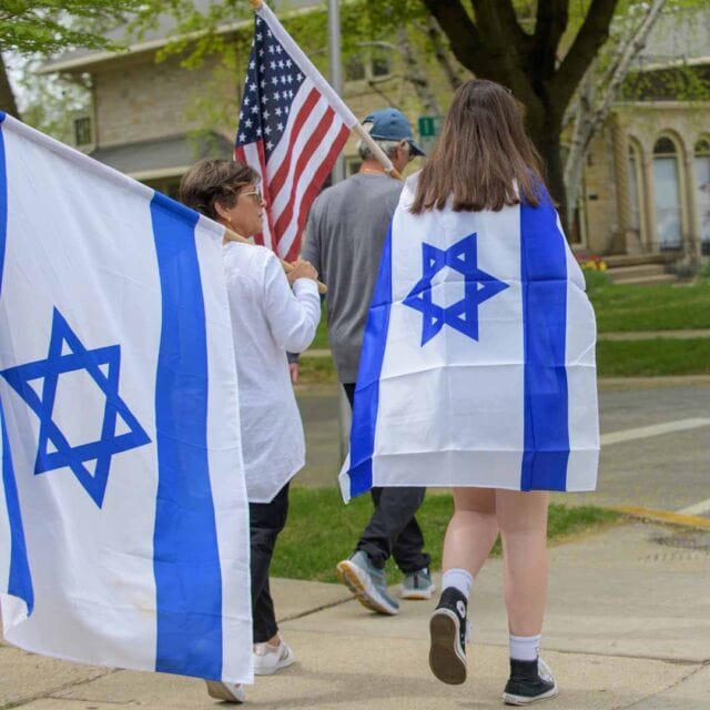 A group of people walking down the street with israeli and american flags.