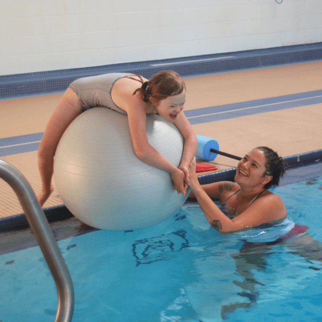 A girl is playing with a ball in a swimming pool.