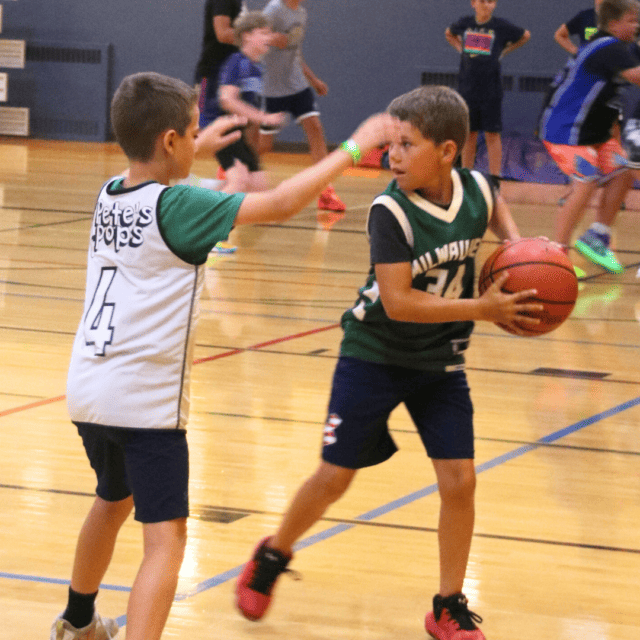 Two young boys playing basketball in a gym.