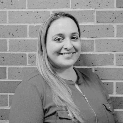 A person smiling while standing in front of a brick wall. Black and white image.