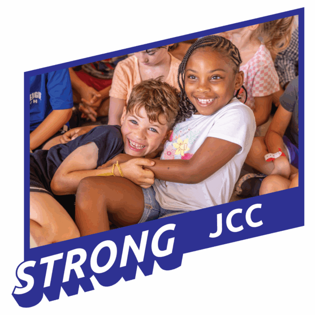 Two smiling children sitting close together in a group, with the word "STRONG" and "JCC" in bold text at the bottom of the image.